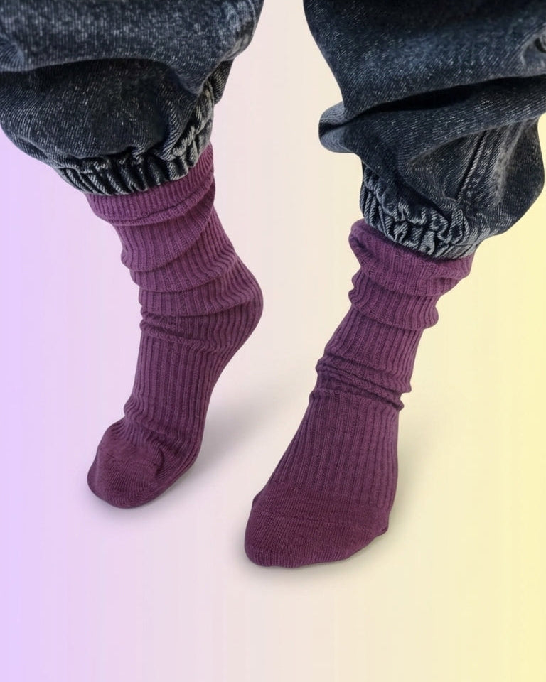 A close-up of a childs's feet wearing dark jeans and plum purple ribbed slouch socks.