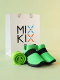 A pair of neon green and black kids shoes with matching rolled-up neon green socks, displayed in front of a white gift bag printed with the brand name 'MIX KIX' on a pale yellow-green background.