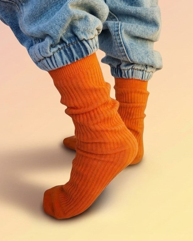 A close-up of kids feet wearing bright orange ribbed slouch socks make from 100% cotton. 
