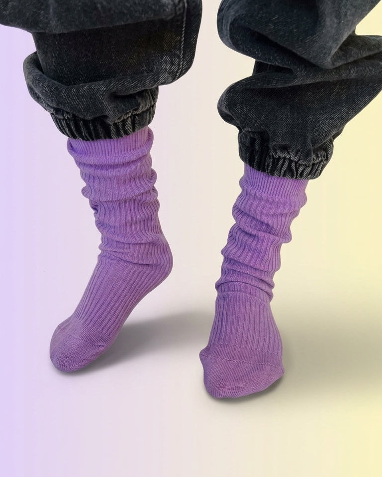 A close-up of a childs feet wearing purple ribbed cotton slouch socks with dark gray cuffed jeans. 