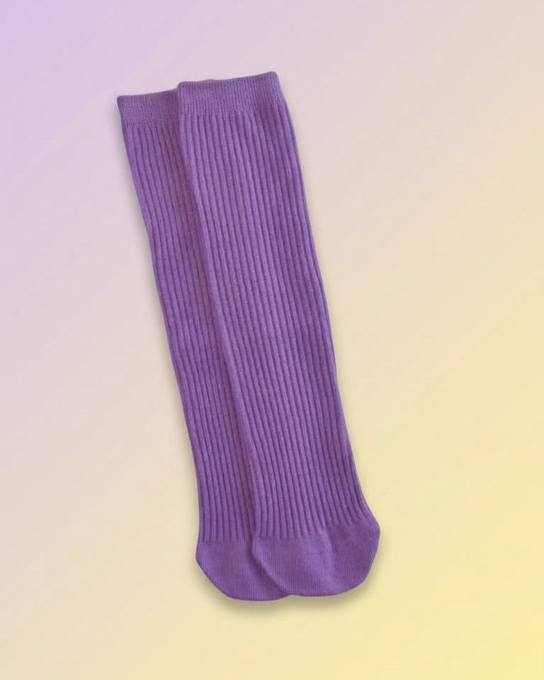 A pair of purple ribbed slouch socks laid flat on a soft pastel gradient background.
